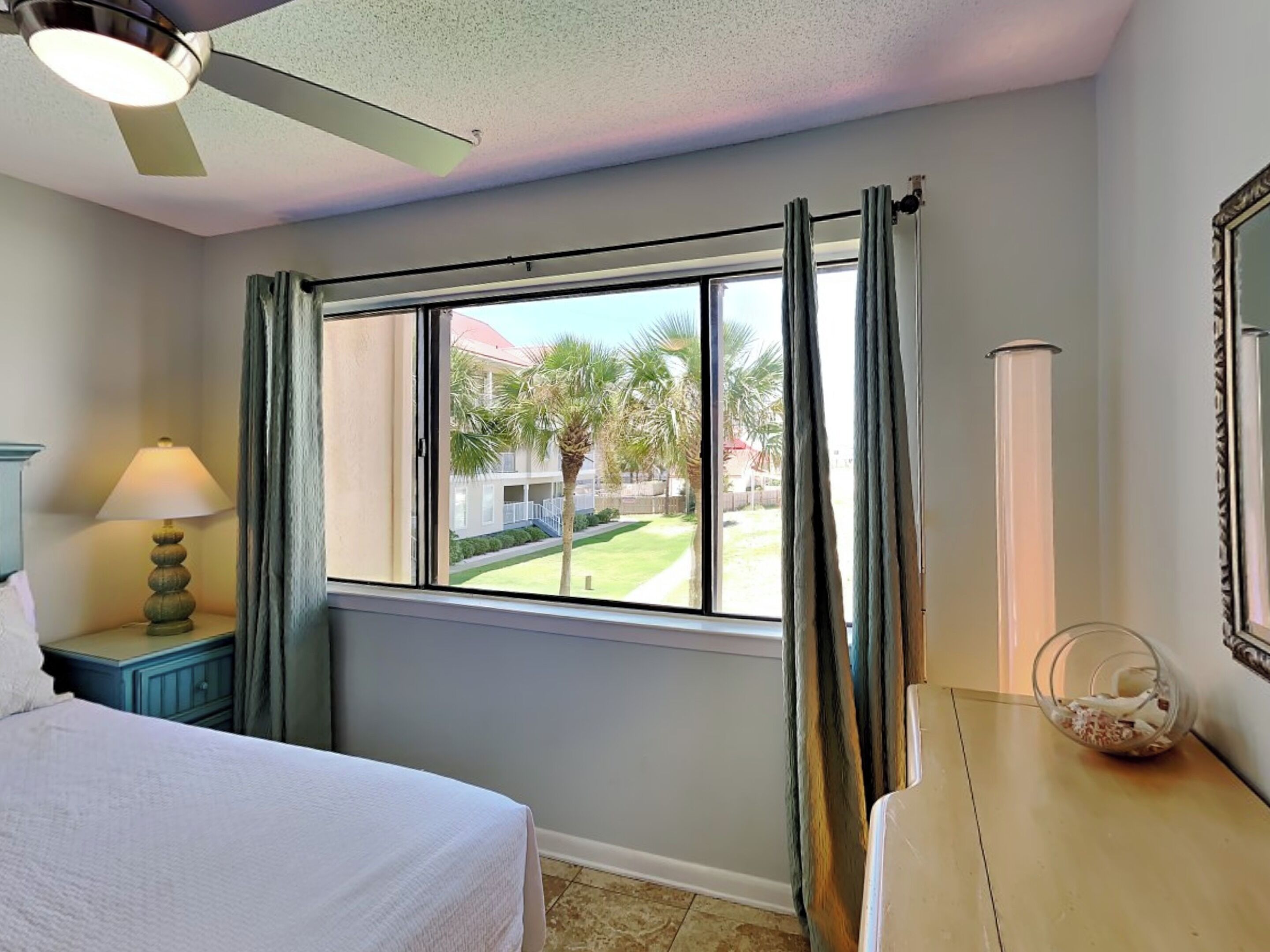 A hotel room with a bed, a nightstand with a lamp, a window with curtains, and a ceiling fan.