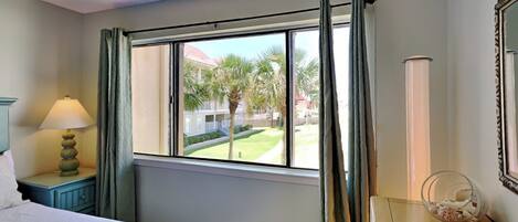 A hotel room with a bed, a nightstand with a lamp, a window with curtains, and a ceiling fan.