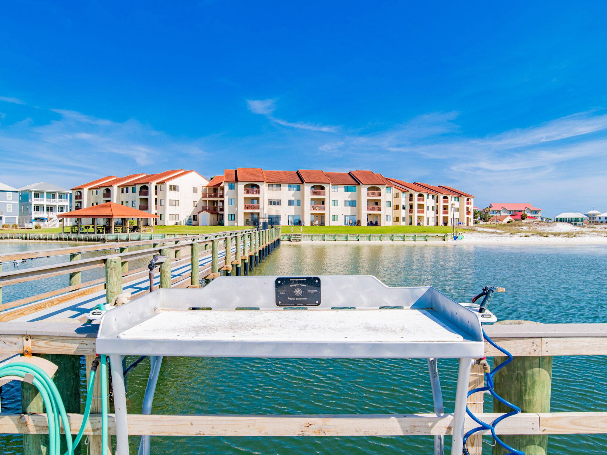 A waterfront view of a multi-story hotel with balconies, a dock, and a clear blue sky.