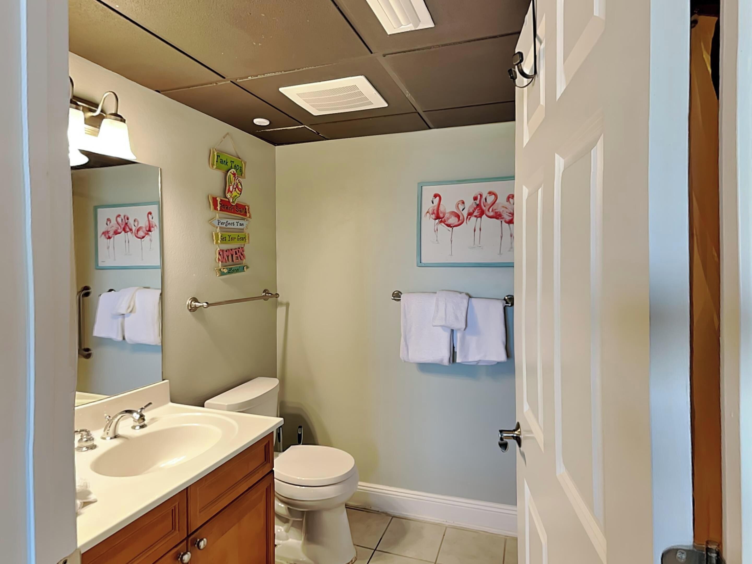 A bathroom with a sink, toilet, and towel racks. There are wall decorations including flamingos and a sign that says "Fank Taps".