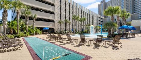 A courtyard with a shuffleboard court, lounge chairs, and a pool area.