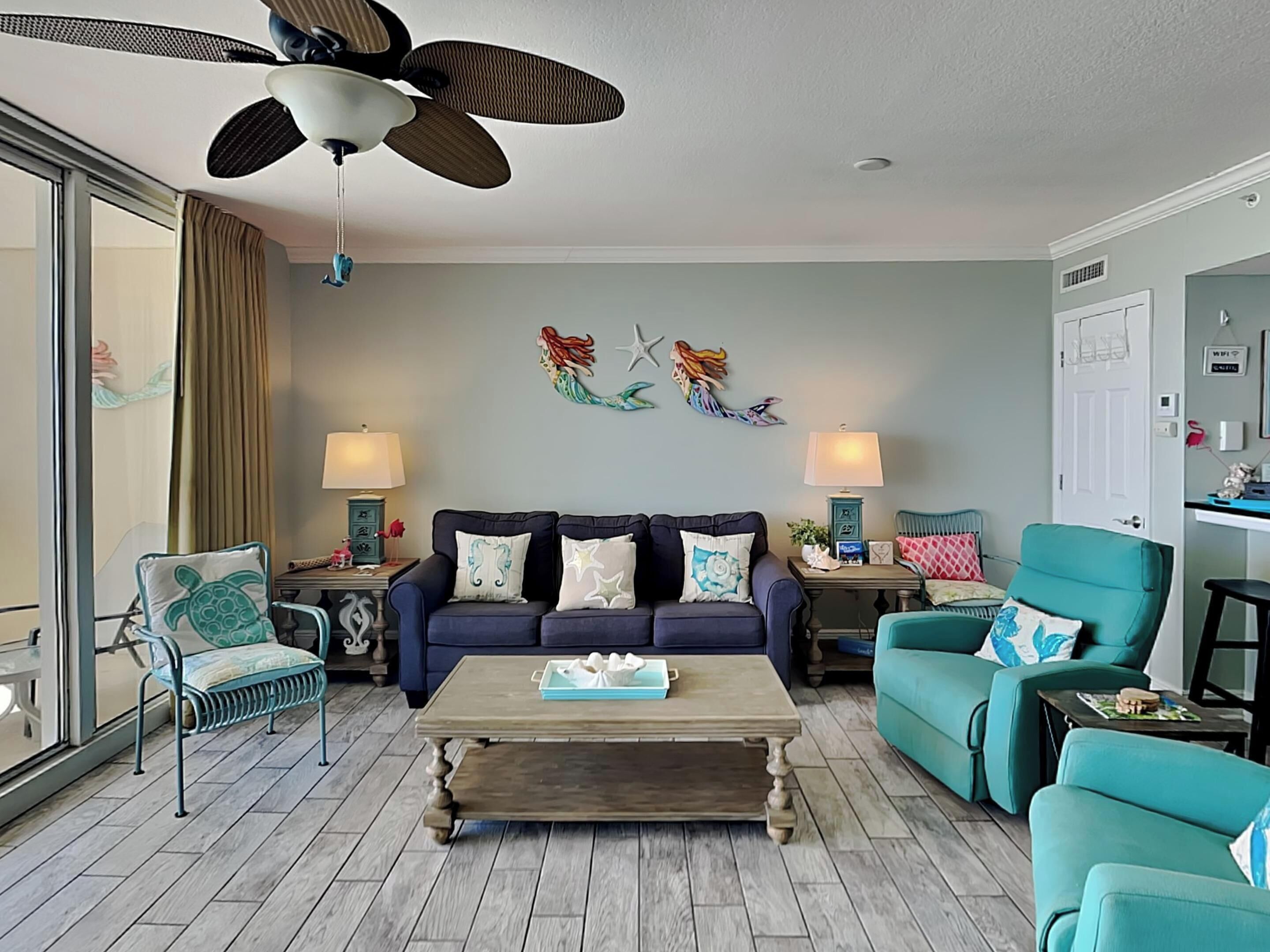 A living room with a ceiling fan, two sofas, a coffee table, and a teal armchair.