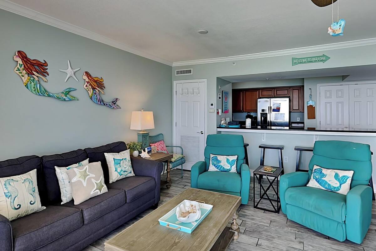 A living room with a sofa, two armchairs, a coffee table, and a kitchen in the background.