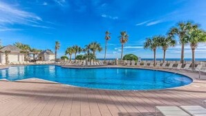 Un área de piscina con sillones de descanso y palmeras, rodeada por una terraza de madera.