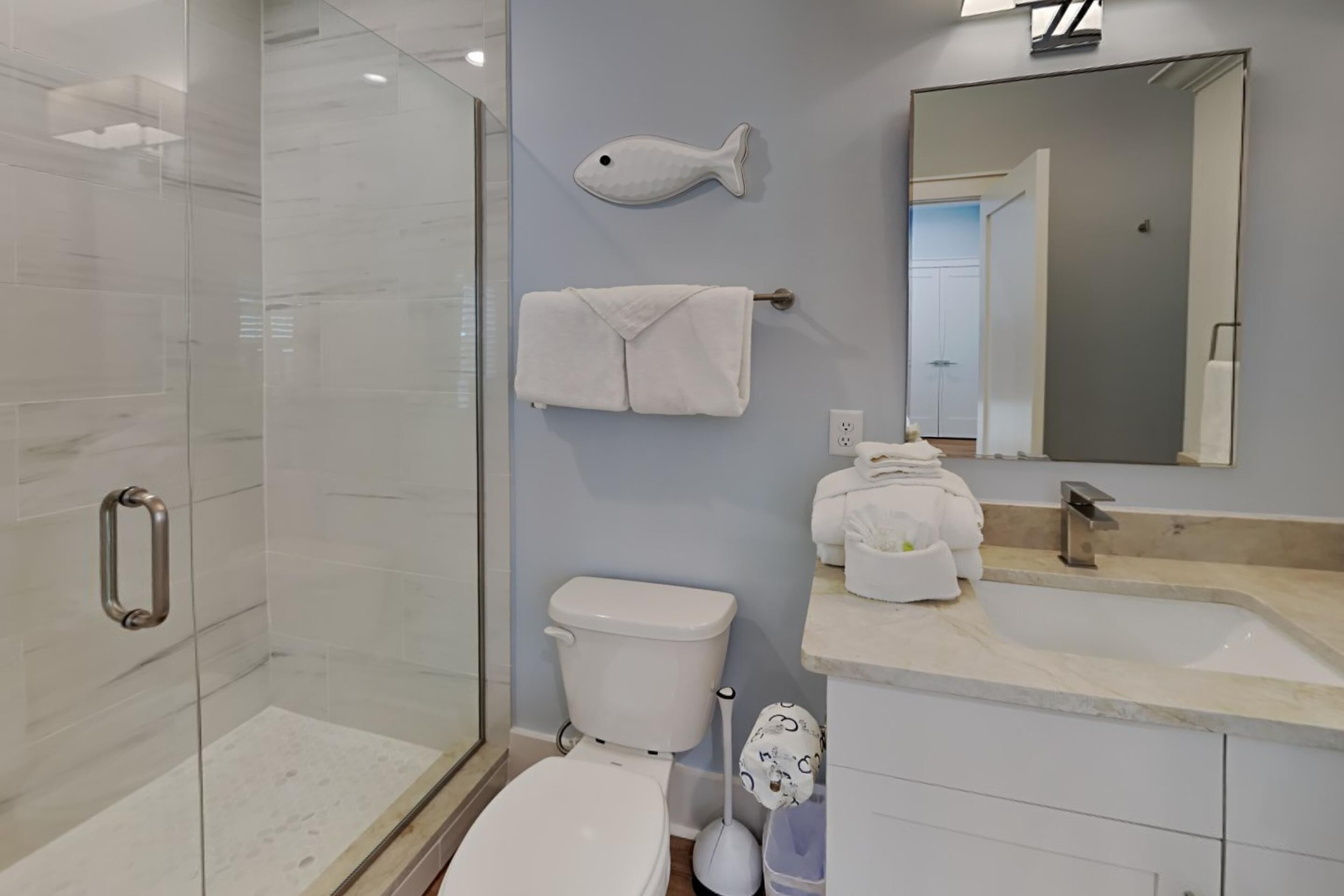 Ein modernes Badezimmer mit einer Duschkabine aus Glas, Toilette, Waschbecken mit Spiegel und einem Handtuchhalter mit Handtüchern.