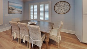 Un coin repas avec une table en bois et des chaises en osier, une fenêtre avec des volets et un élément décoratif mural.