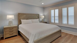 Une chambre avec un grand lit, deux tables de chevet avec des lampes, un plancher en bois et une fenêtre avec des stores.