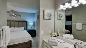 Une chambre d’hôtel moderne, équipée d’un lit, d’une table de chevet, d’une lampe et d’un grand miroir avec des lumières au-dessus du lavabo.