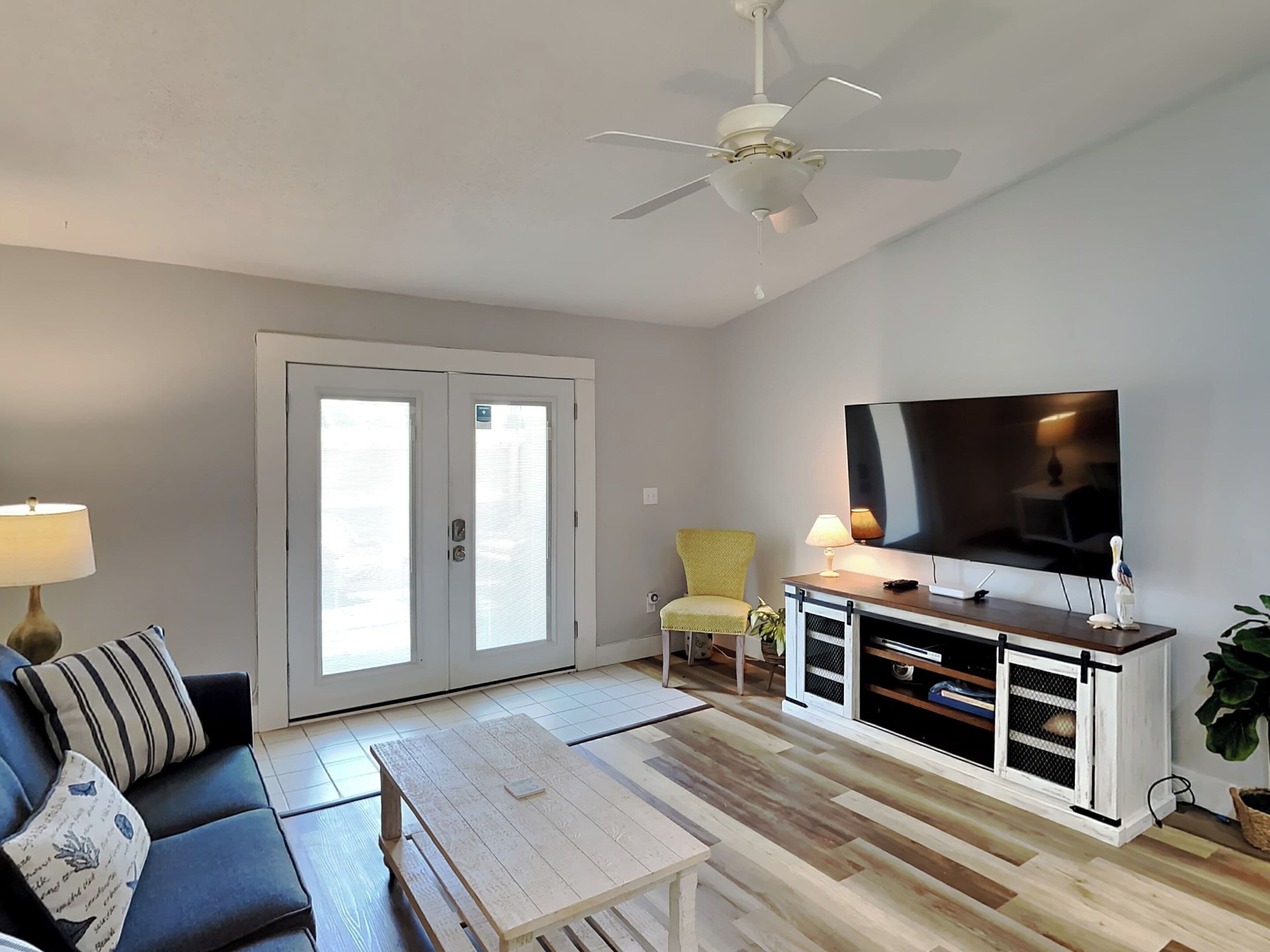 A living room with a sofa, coffee table, TV, and a ceiling fan.