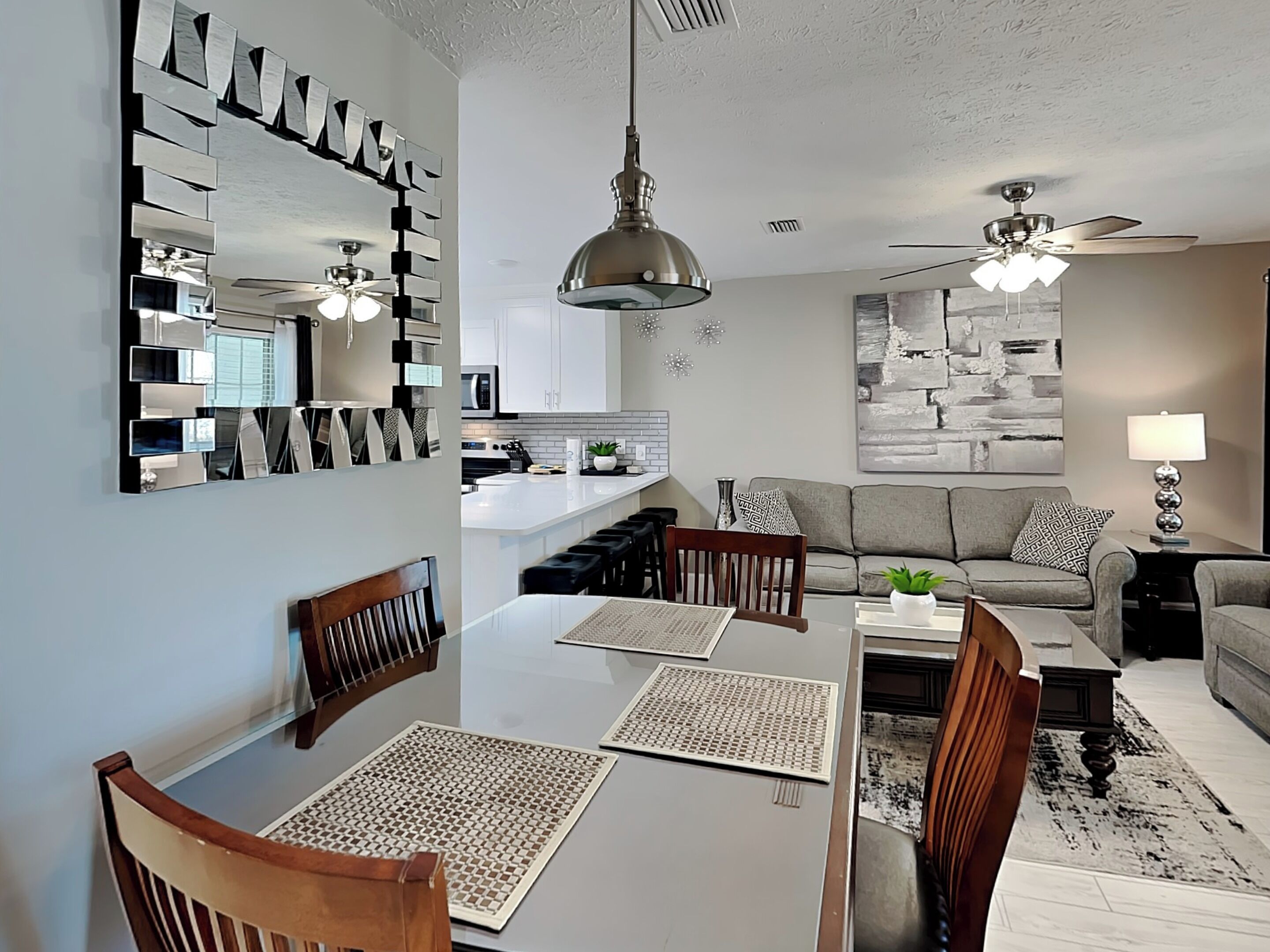 A modern living room with a dining area, a kitchen, and a ceiling fan.