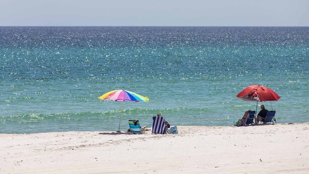 Una playa con dos sombrillas y gente descansando en la arena.