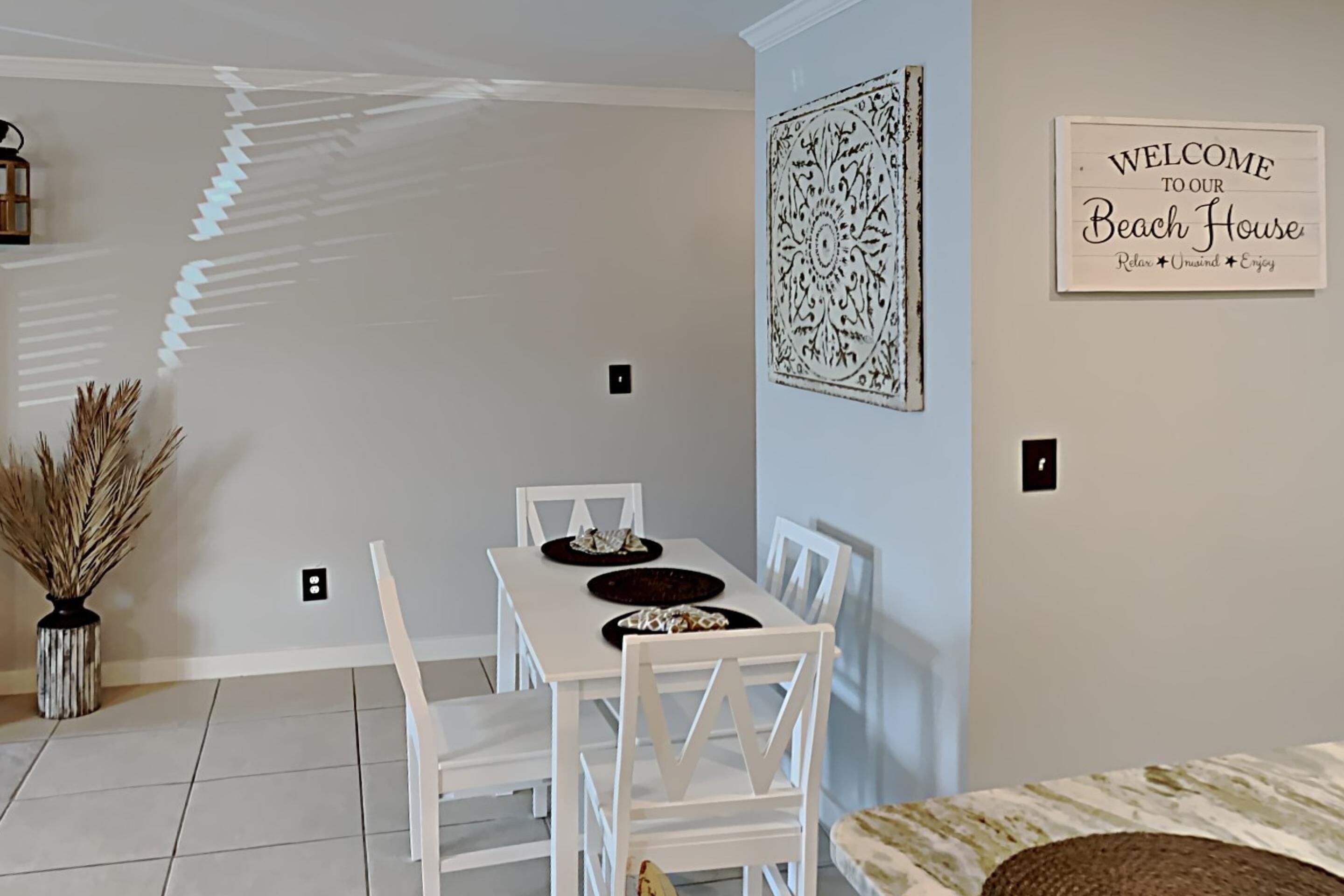 A dining area with a white table and chairs, a decorative wall piece, and a welcome sign.