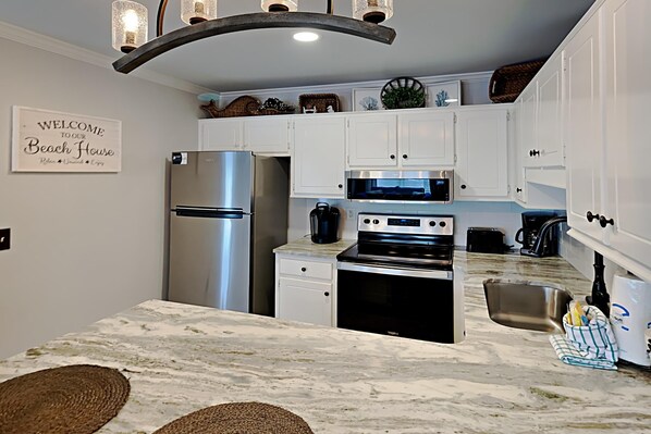 A modern kitchen with white cabinets, stainless steel appliances, and a marble countertop.