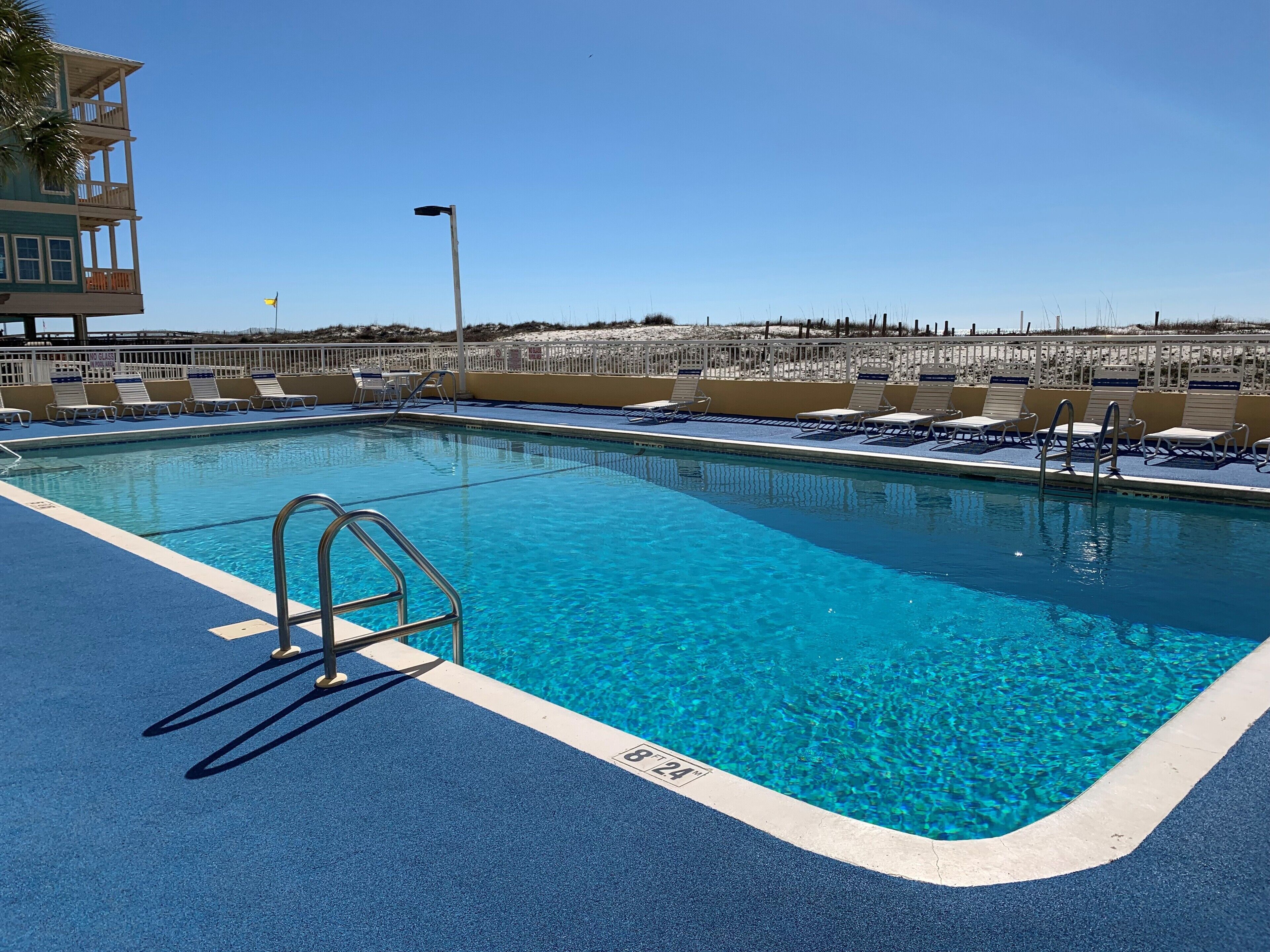 Une piscine d’eau cristalline, avec un poste de surveillance pour les sauveteurs, des chaises longues et une vue sur la plage.