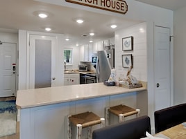 A modern kitchen with white cabinets, a stainless steel refrigerator, and a bar area with stools.
