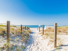 A sandy beach path leading to the ocean, marked by wooden posts and ropes.
