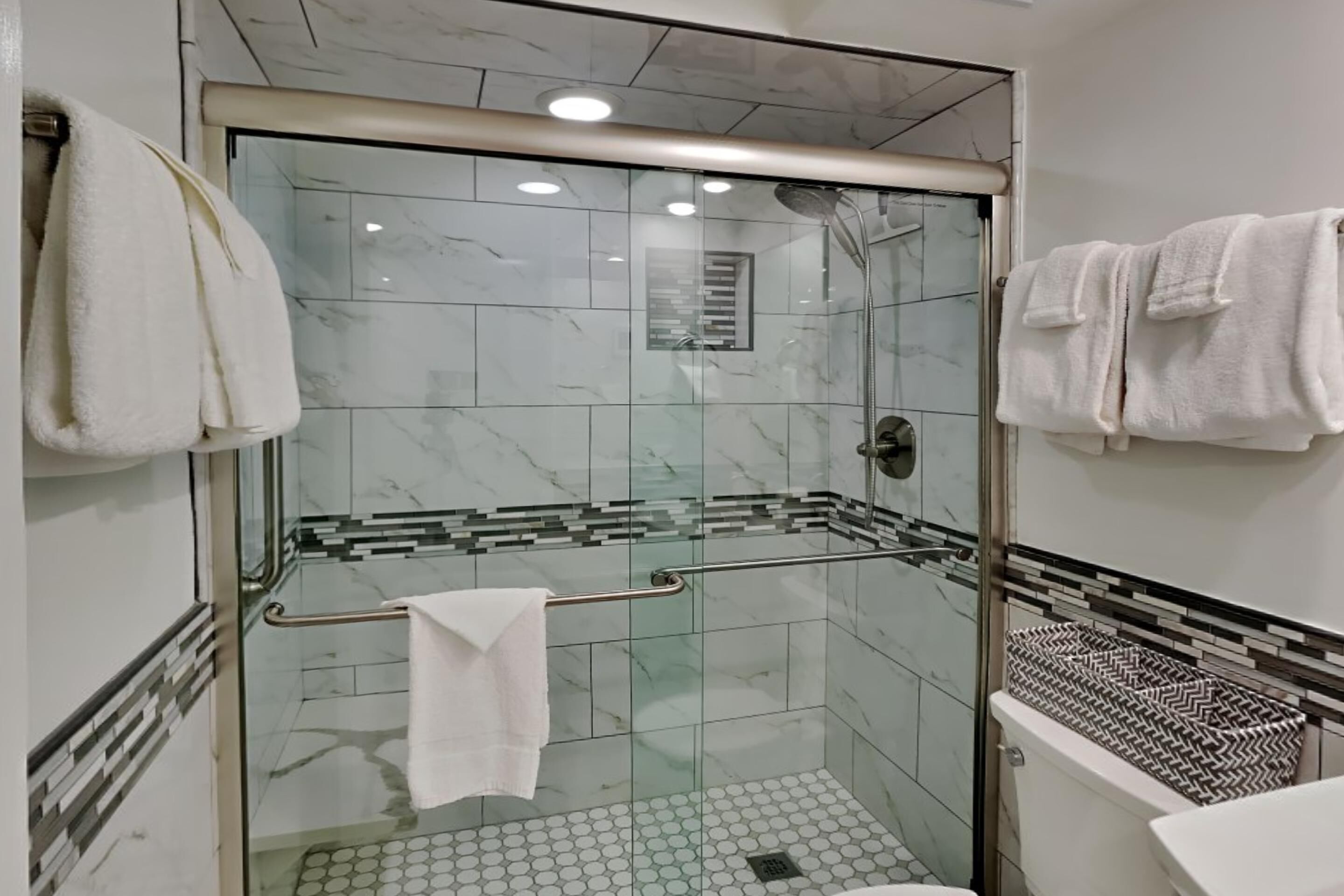 A modern bathroom with a glass-enclosed shower, white marble tiles, and a white toilet.