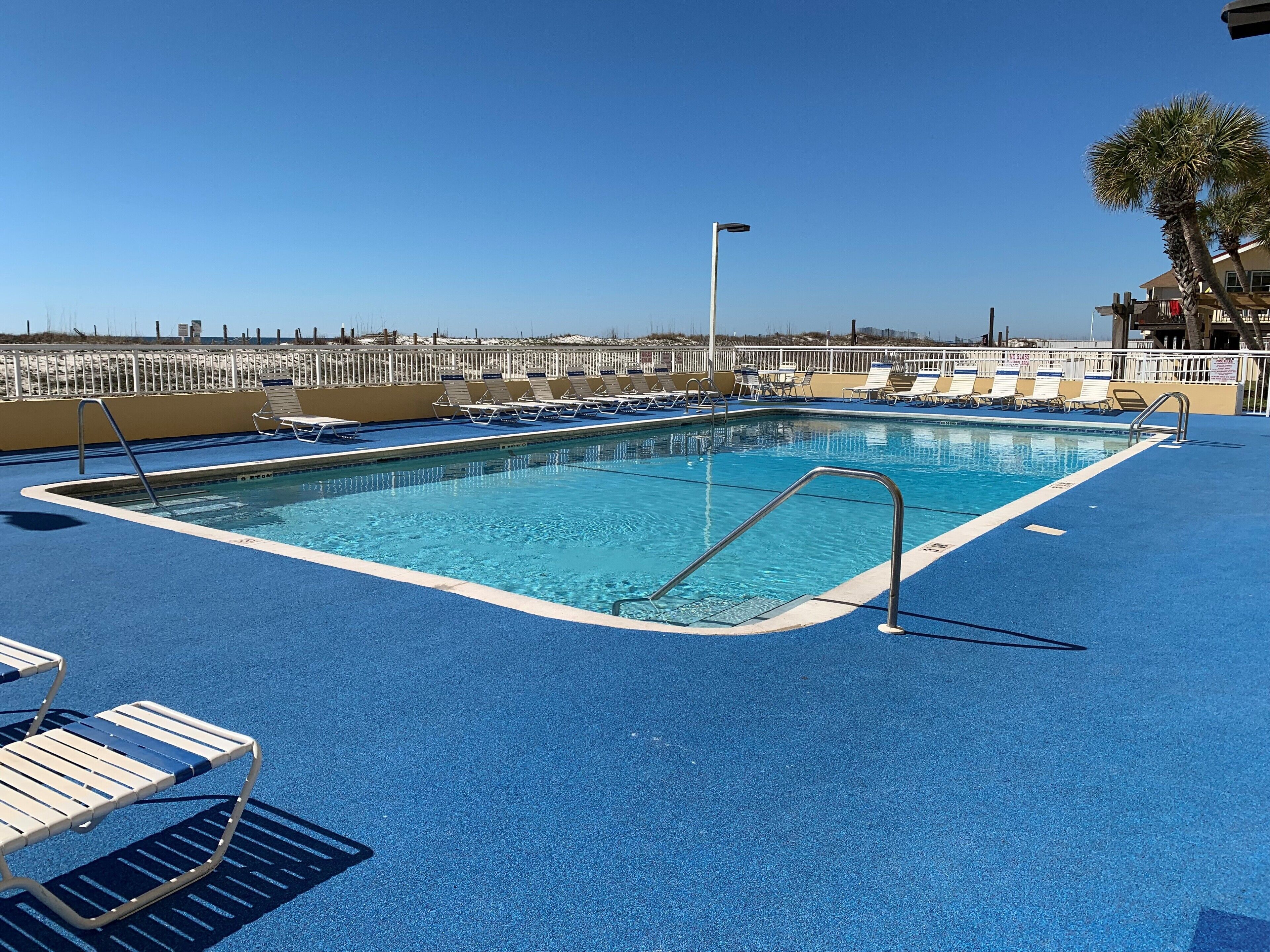 A swimming pool with blue deck and lounge chairs, surrounded by a white fence.