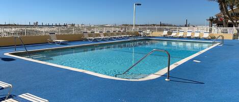 A swimming pool with blue deck and lounge chairs, surrounded by a white fence.