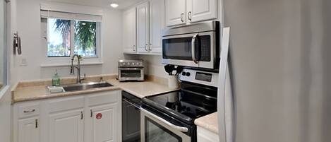 A modern kitchen with white cabinets, a stainless steel refrigerator, a built-in oven, a microwave, and a toaster oven.
