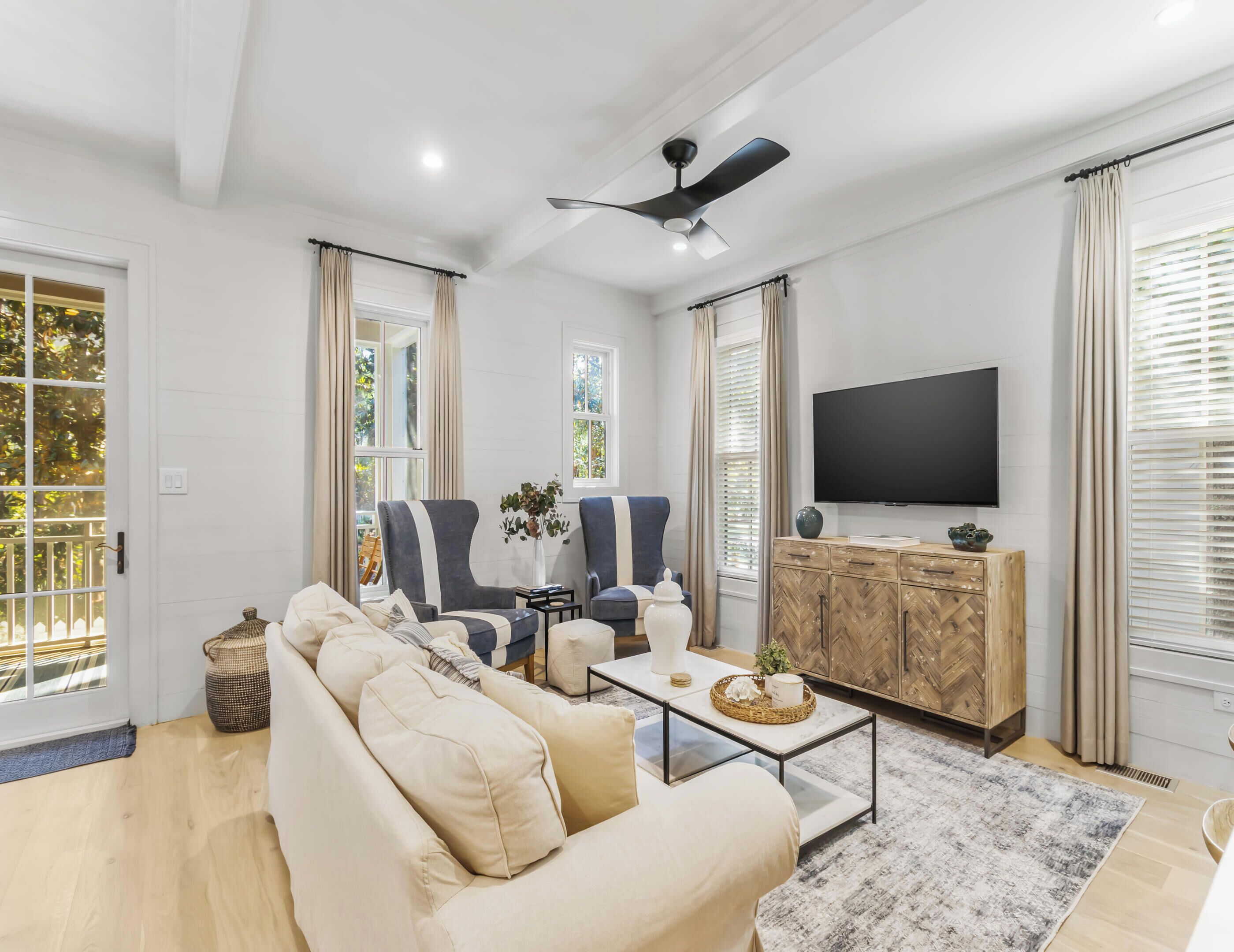 A modern living room with a beige sofa, two armchairs, a coffee table, and a TV on a wooden cabinet.