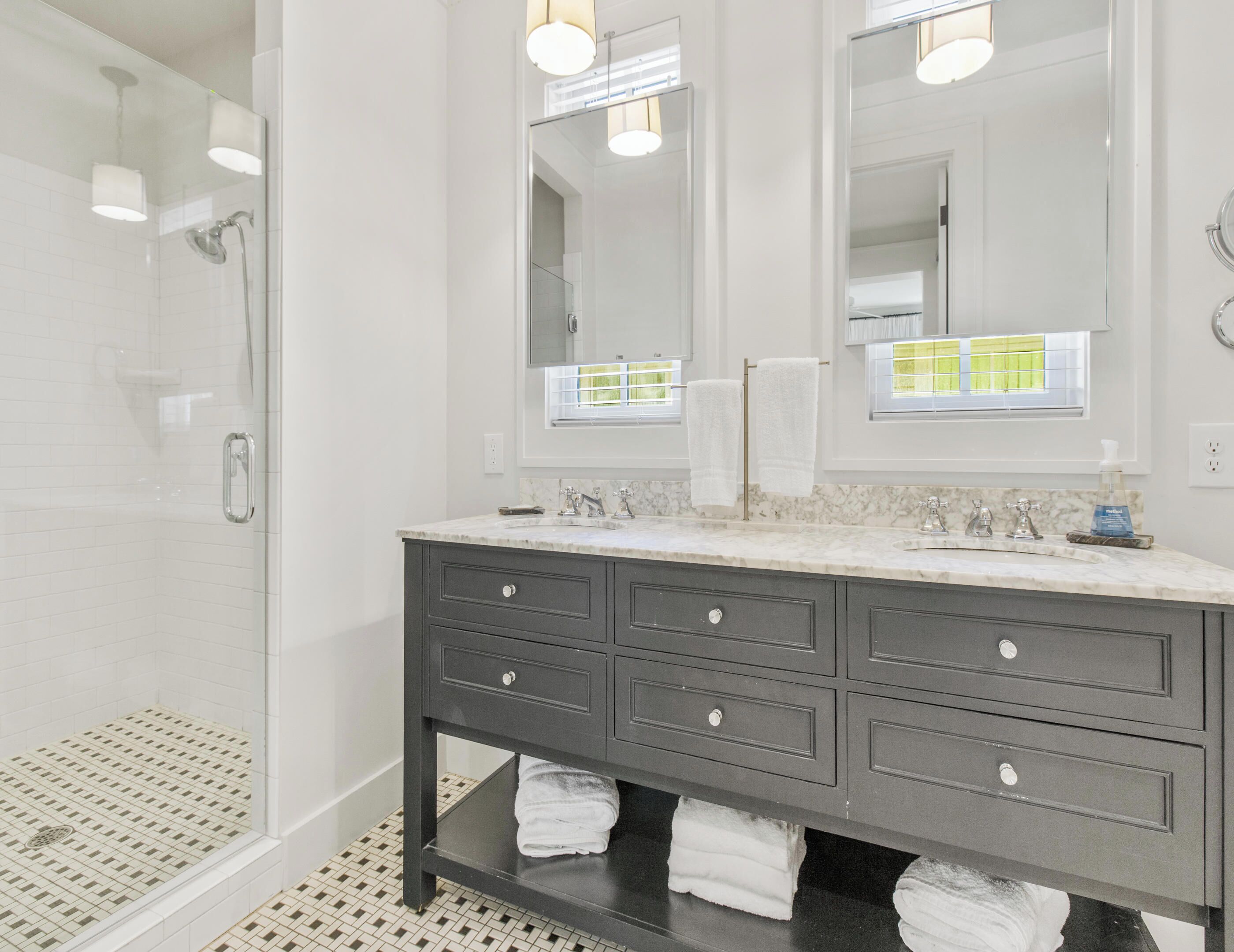 A modern bathroom with a glass shower enclosure, a dark vanity with multiple drawers, and a large mirror above the sink.