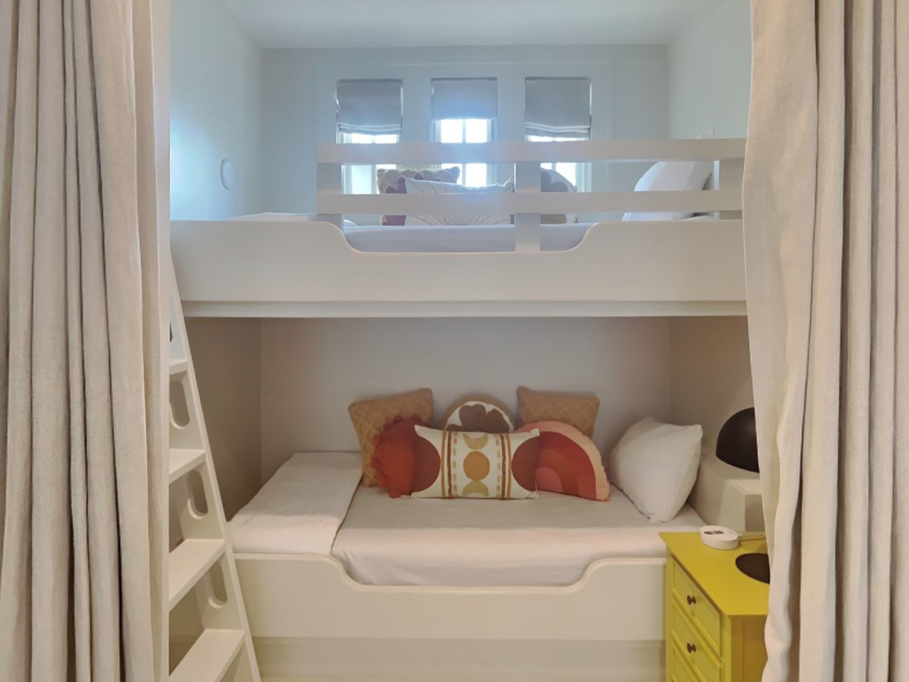 A bunk bed room with a white headboard, a small desk, and a yellow dresser.