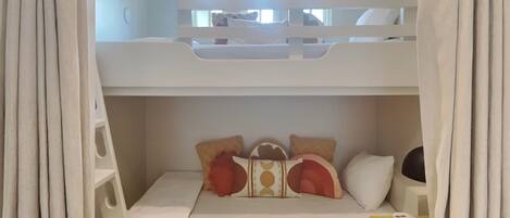 A bunk bed room with a white headboard, a small desk, and a yellow dresser.