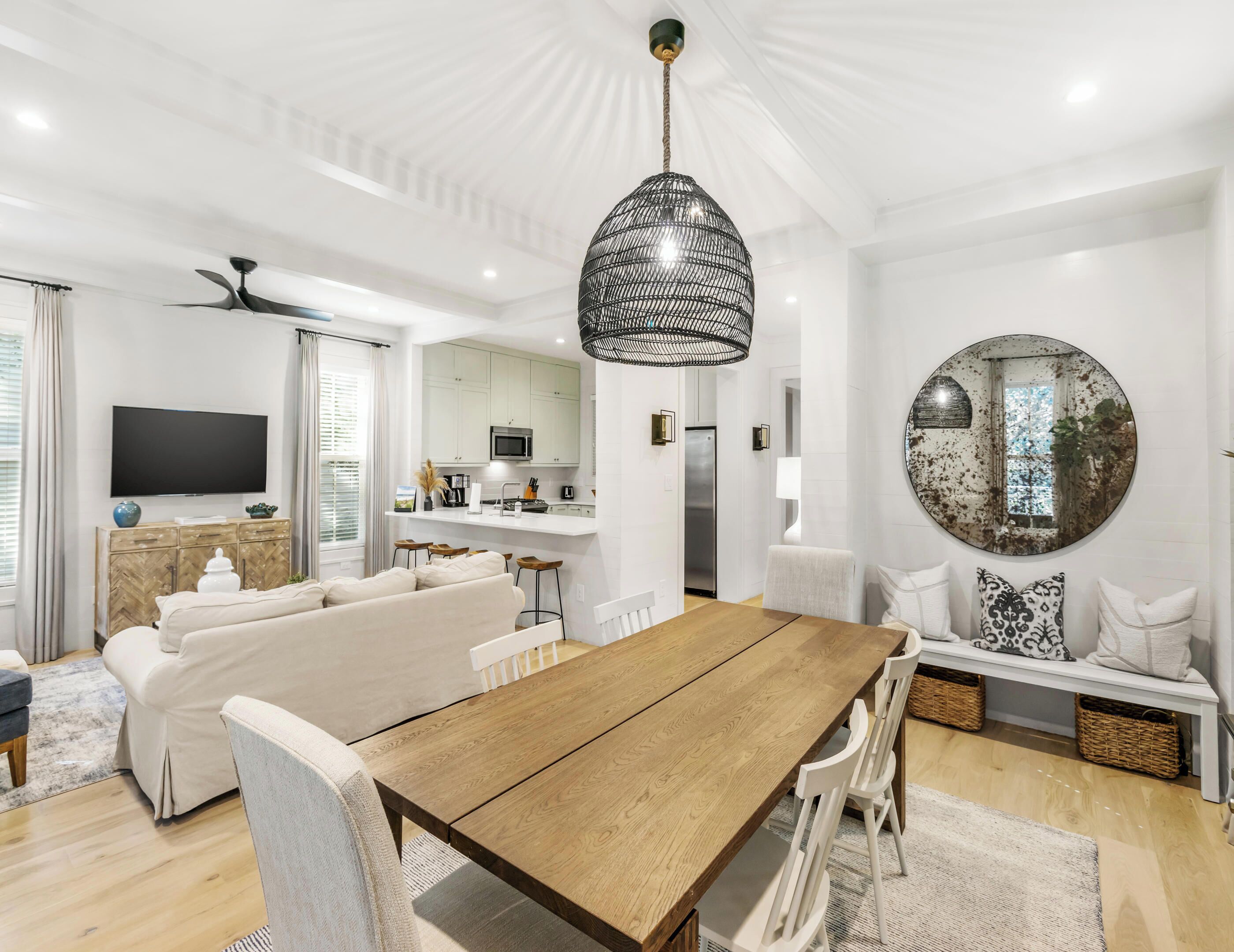 A modern living room with a wooden dining table, white sofas, and a kitchen area in the background.
