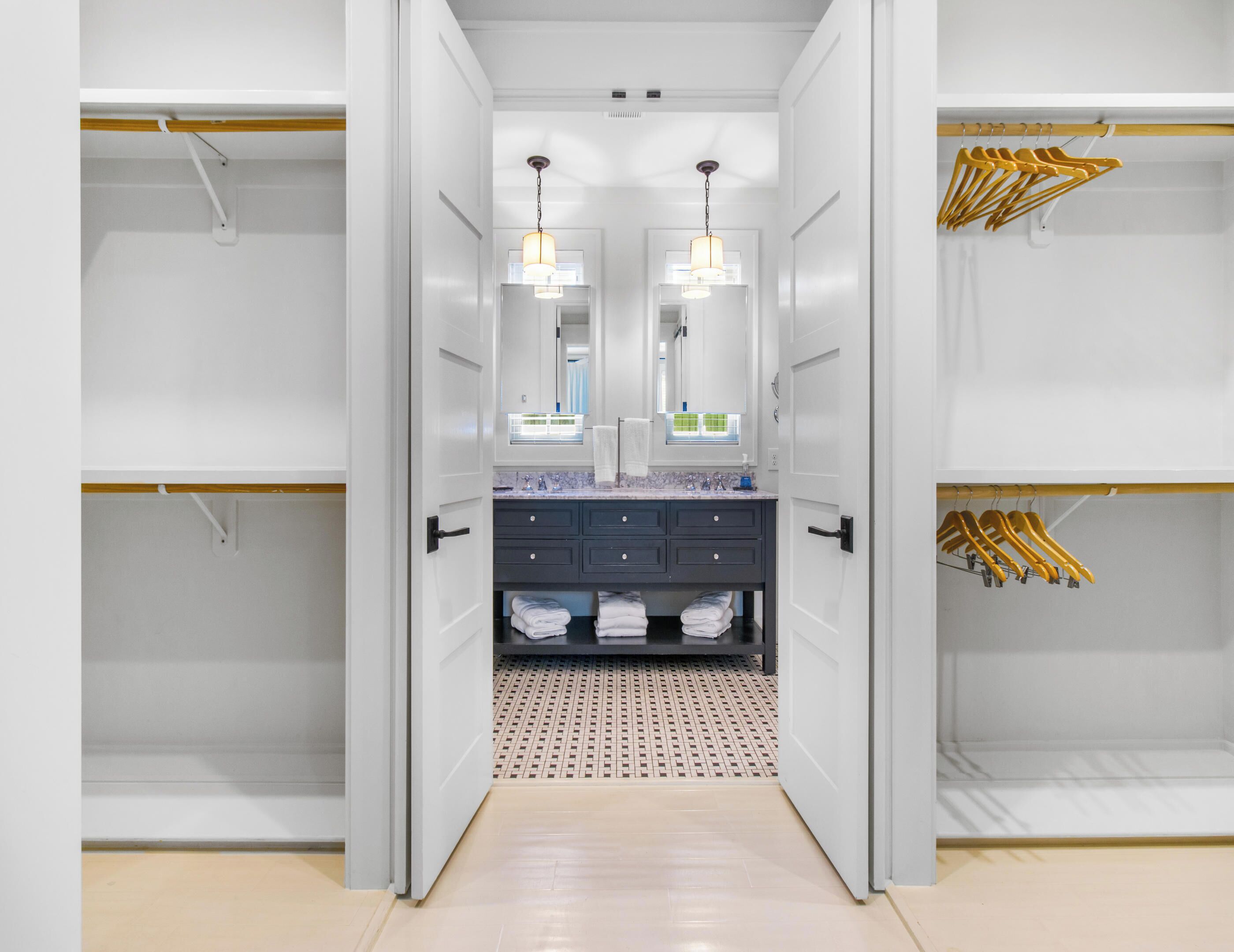 A walk-in closet with a mirrored vanity, hanging clothes, and a patterned floor.
