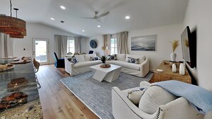 A spacious living room with a large sofa set, a coffee table, and a dining area with a long table. - Seaspray by Southern Vacation Rentals (Miramar Beach)