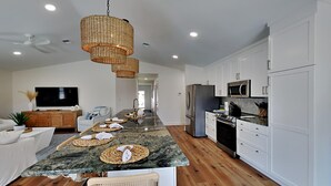 A modern kitchen with white cabinets, a granite countertop, and a dining area with a bench and woven placemats. - Seaspray by Southern Vacation Rentals (Miramar Beach)
