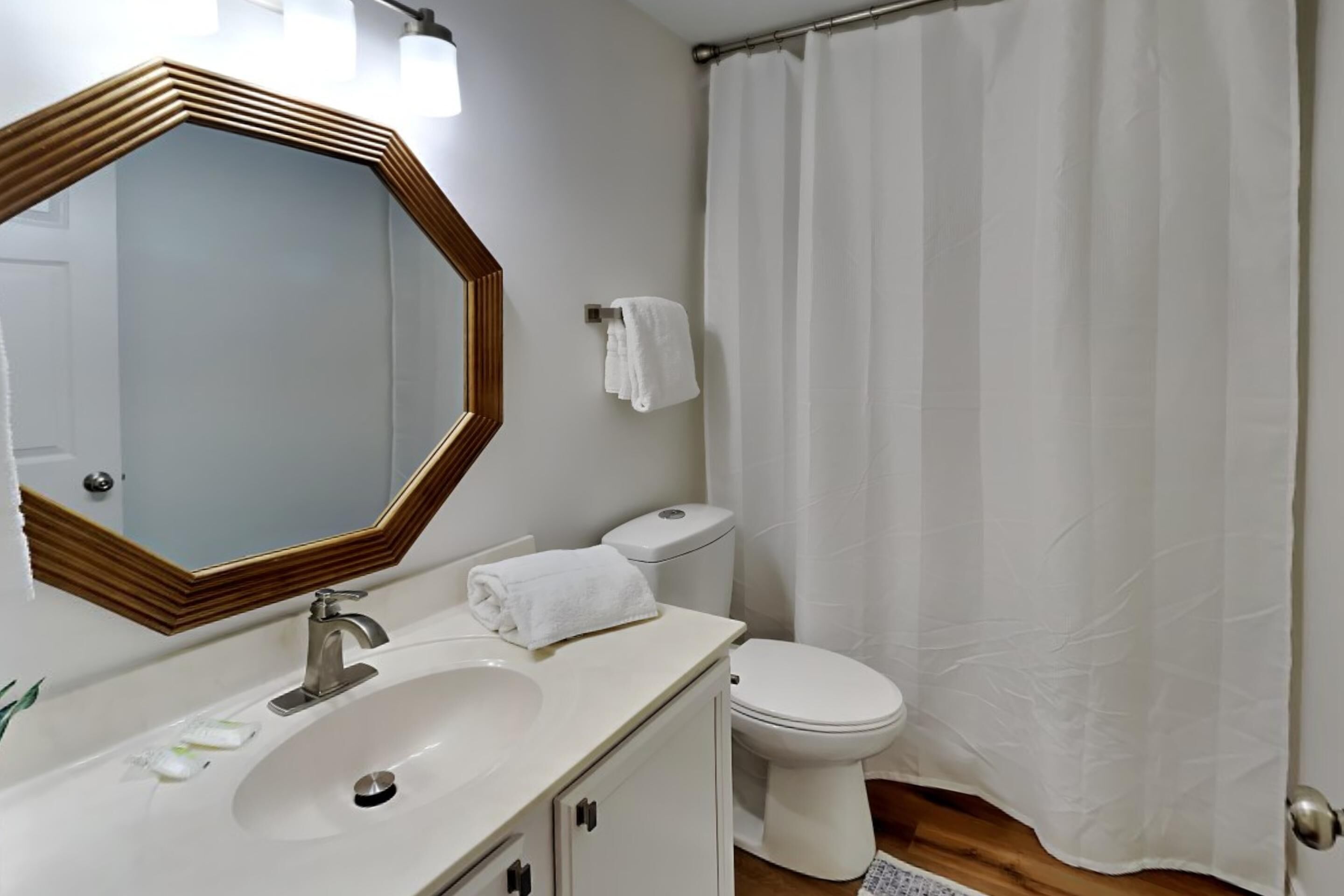 Une salle de bain équipée d’un lavabo, d’un miroir, de toilettes et d’un rideau de douche.