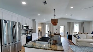 A modern kitchen with a central island, stainless steel appliances, and a dining area with a sofa and rug. - Seaspray by Southern Vacation Rentals (Miramar Beach)
