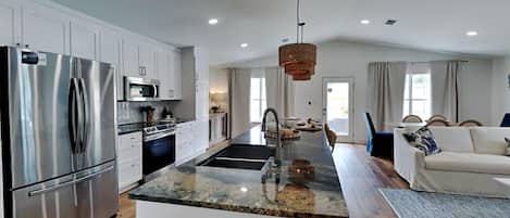A modern kitchen with a central island, stainless steel appliances, and a dining area with a sofa and rug.