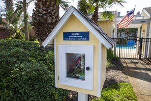 Una pequeña biblioteca amarilla con un letrero que dice "Seaspray Little Free Library" y una bandera estadounidense.