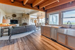 Relax in a spacious open-plan living area with a comfortable sofa set and dining table, surrounded by a large window offering a view of the surrounding landscape.
