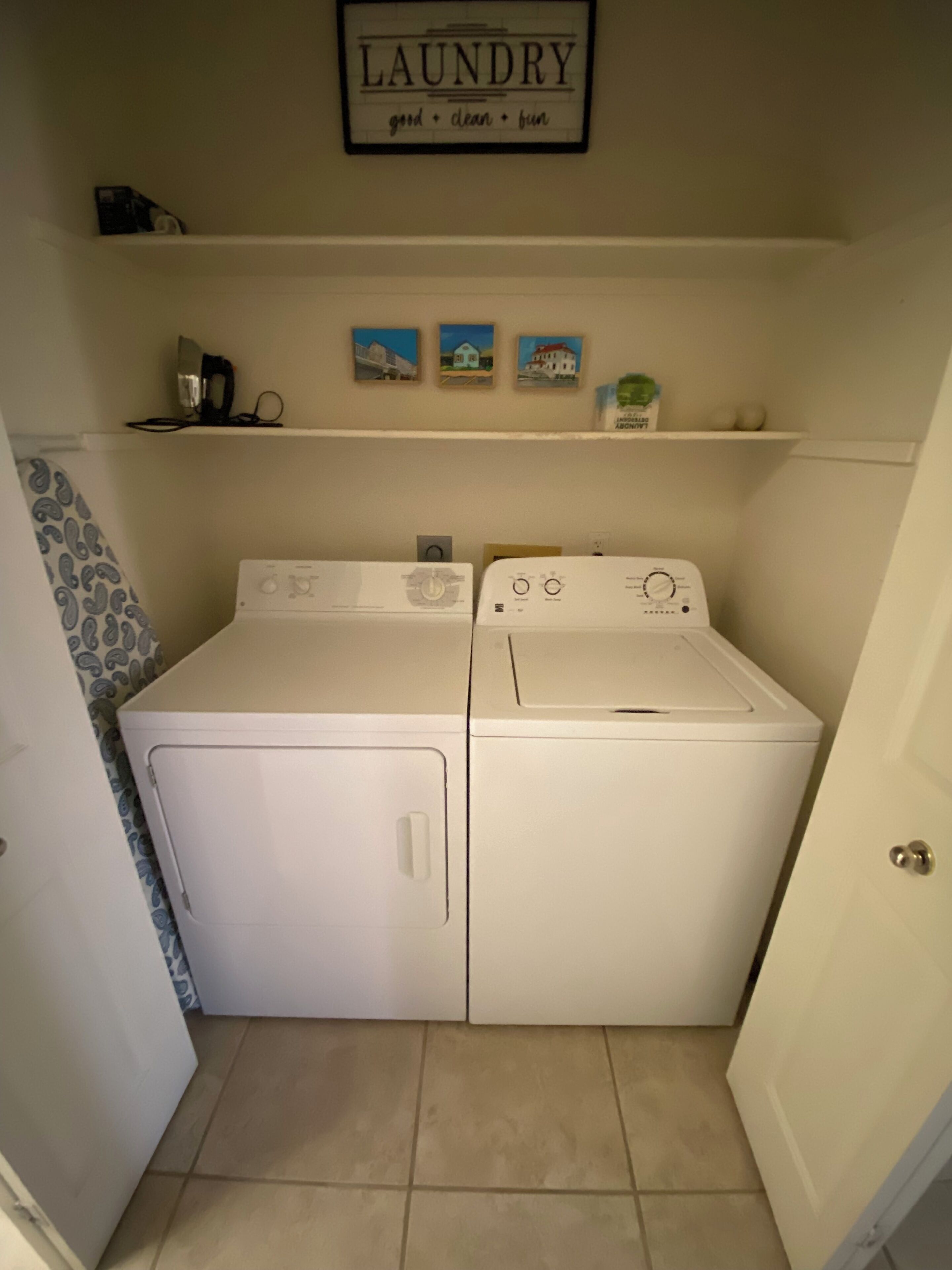 A laundry room with two white washing machines, a shelf with decorative items, and a framed sign above stating "laundry good clean fun".