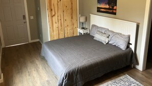 A bedroom with a bed, a nightstand, a lamp, a wooden wardrobe, and a painting on the wall.