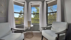 A corner room with three windows, a small round table, two chairs, and a view of trees and a balcony. - Mountain Retreat | Hot Tub & Fire Pit (Prescott)