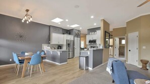 A modern kitchen with white cabinets, a central island, and a dining area with blue chairs. - Mountain Retreat | Hot Tub & Fire Pit (Prescott)