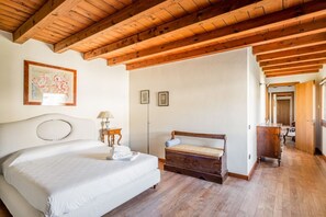 A bedroom with a bed, wooden ceiling beams, a bedside table with a lamp, and a wooden bench.