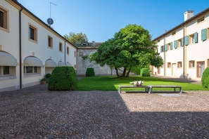 A courtyard with a gravel path, a bench, and a large tree.