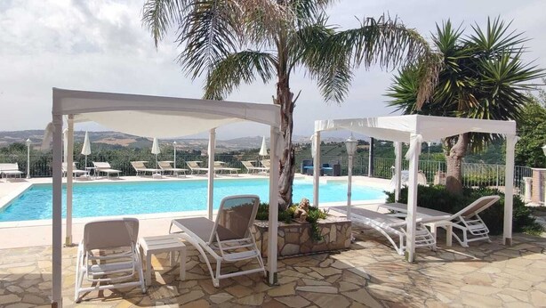 A pool area with lounge chairs and a pergola, surrounded by palm trees and a view of hills. - ROMANTIC PENTHOUSE 7 BEDS (Case Alte)