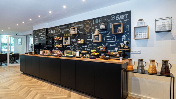 A modern bar area with a chalkboard wall displaying various food and drink options. - Hotel Das Q Spaichingen (Spaichingen)