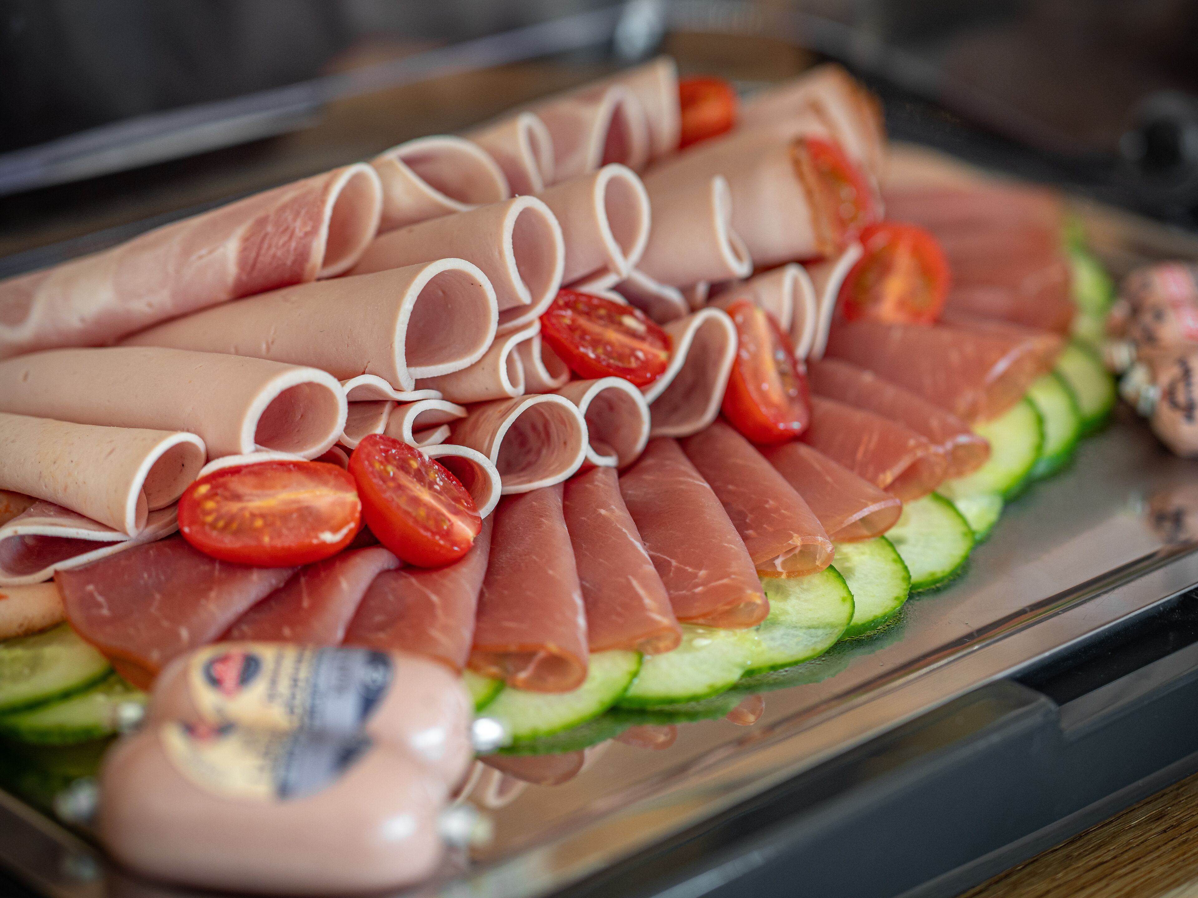 Een charcuterieplank met diverse vleessoorten, tomaten en komkommers.