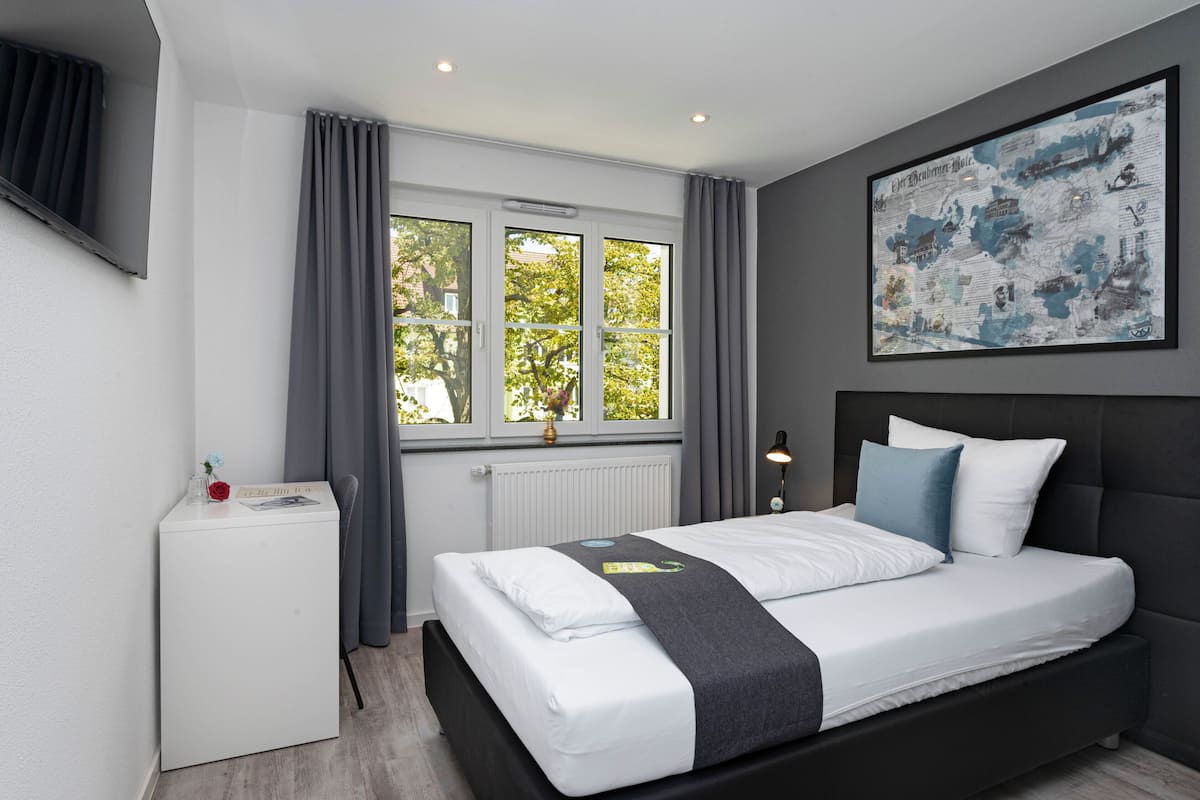 Un dormitorio moderno con una cama grande, una mesita de noche pequeña, un radiador y una ventana con cortinas.