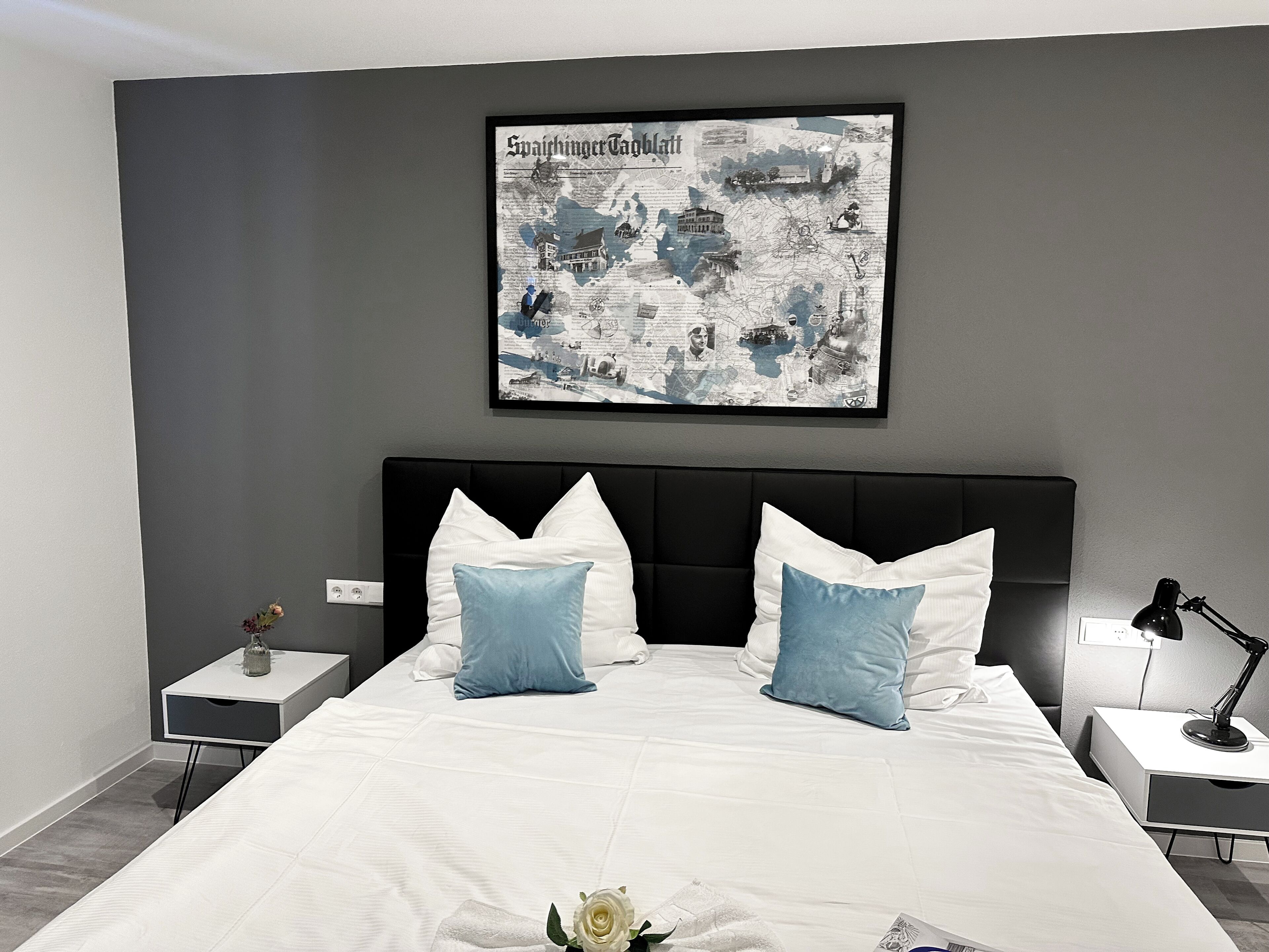 Ein modernes Schlafzimmer mit einem großen Bett, zwei Nachttischen, einer an der Wand befestigten Karte und einer kleinen Vase mit Blumen.