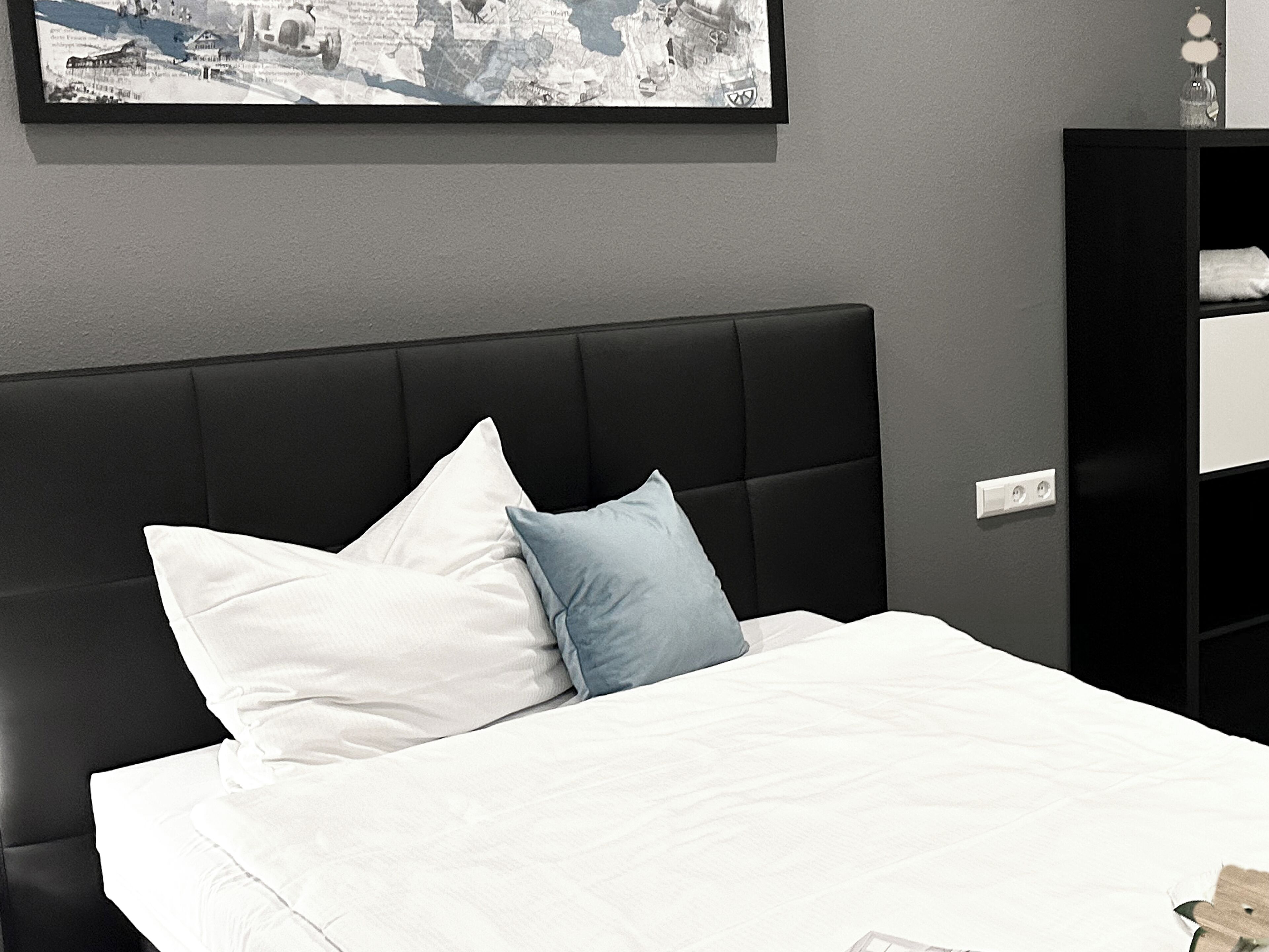 A bedroom with a black upholstered headboard, white bedding, and a framed picture on the wall.