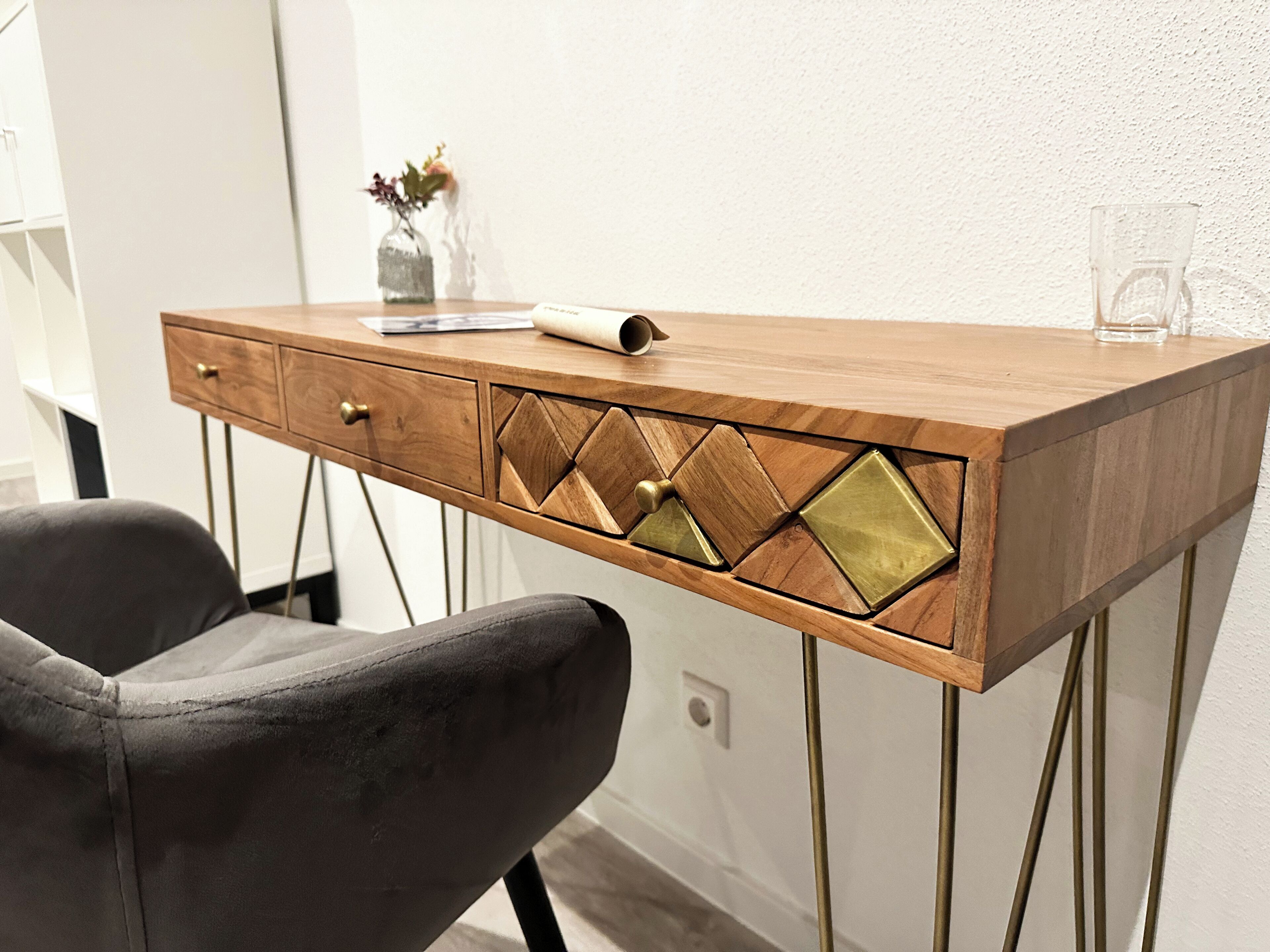 Un bureau en bois avec des tiroirs, un vase rempli de fleurs et un verre posé sur le bureau.